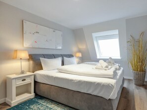 Ein modernes Schlafzimmer mit einem großen Bett, Nachttischlampen, einem kleinen Beistelltisch, einer Wanddekoration und einem Fenster mit Blick.