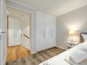 A bedroom with a bed, a nightstand with a lamp, and a wardrobe. - Holiday Apartment With 1 Bedroom (Sylt)