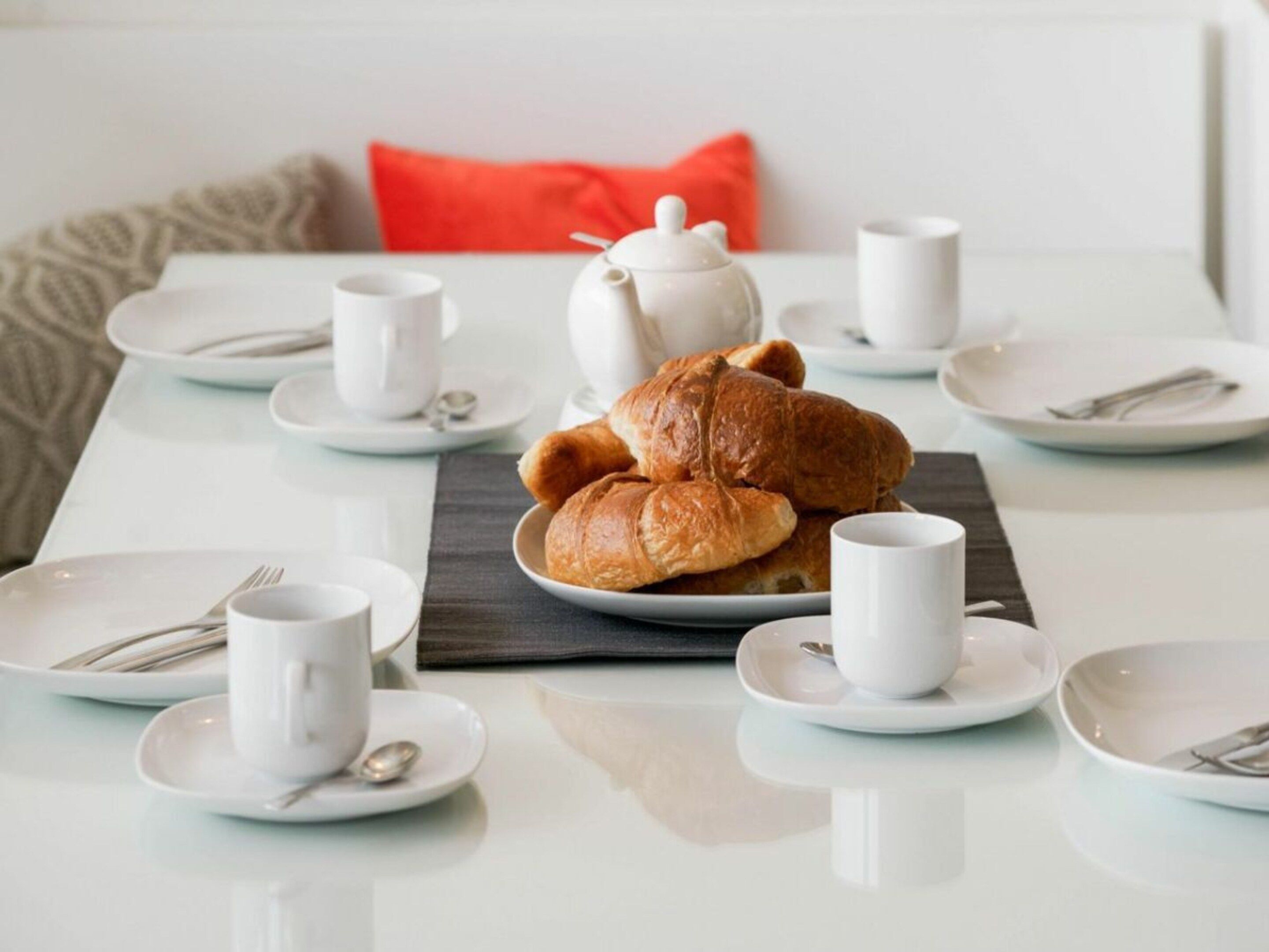 A breakfast setting with croissants, cups, and a teapot on a table.