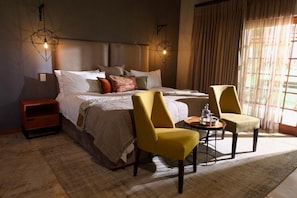Una habitación de hotel con una cama grande, dos sillas, una mesita y una mesita de noche.