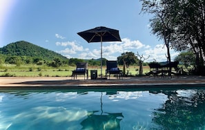 Un área junto a la piscina con sillones de descanso y una sombrilla, rodeada de un paisaje natural.