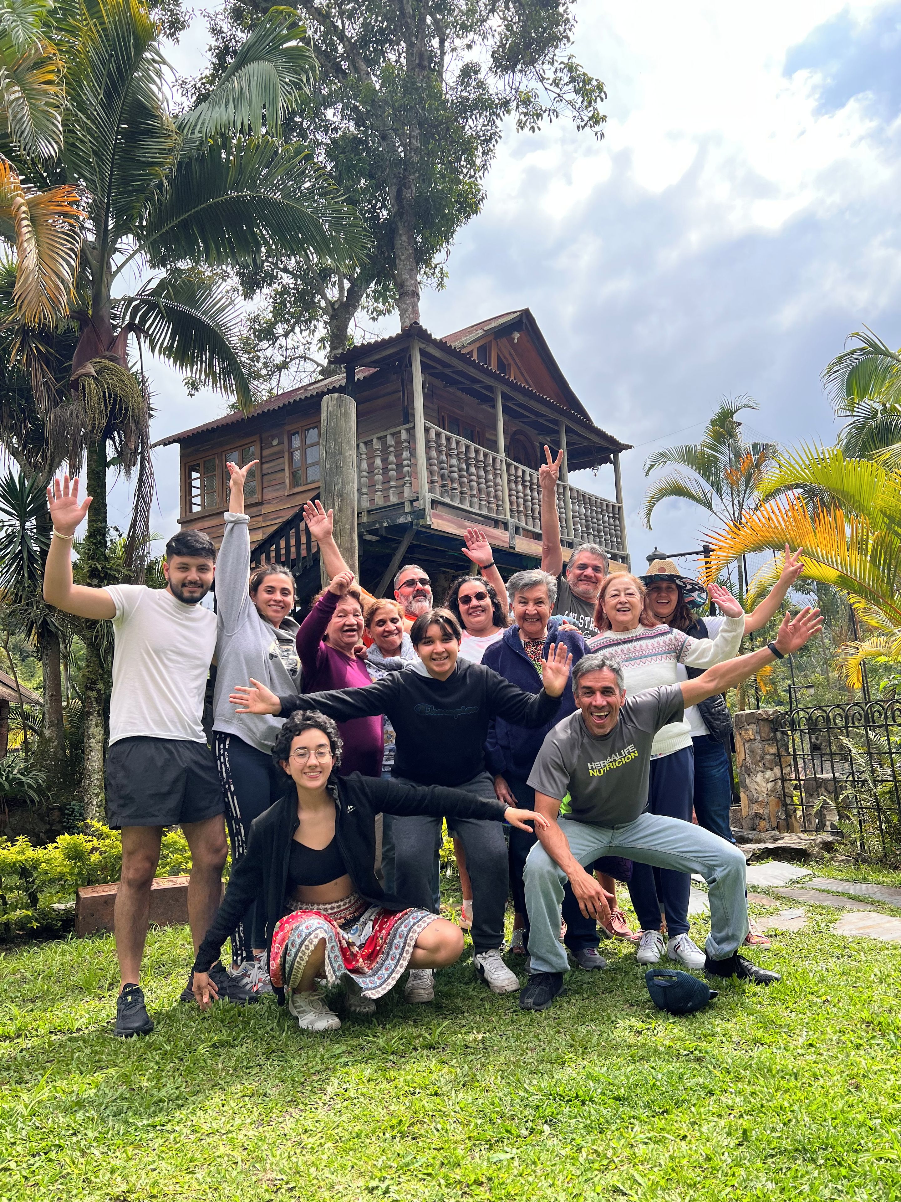 Un grupo de personas posando frente a una casa de madera con balcón, rodeada de vegetación.