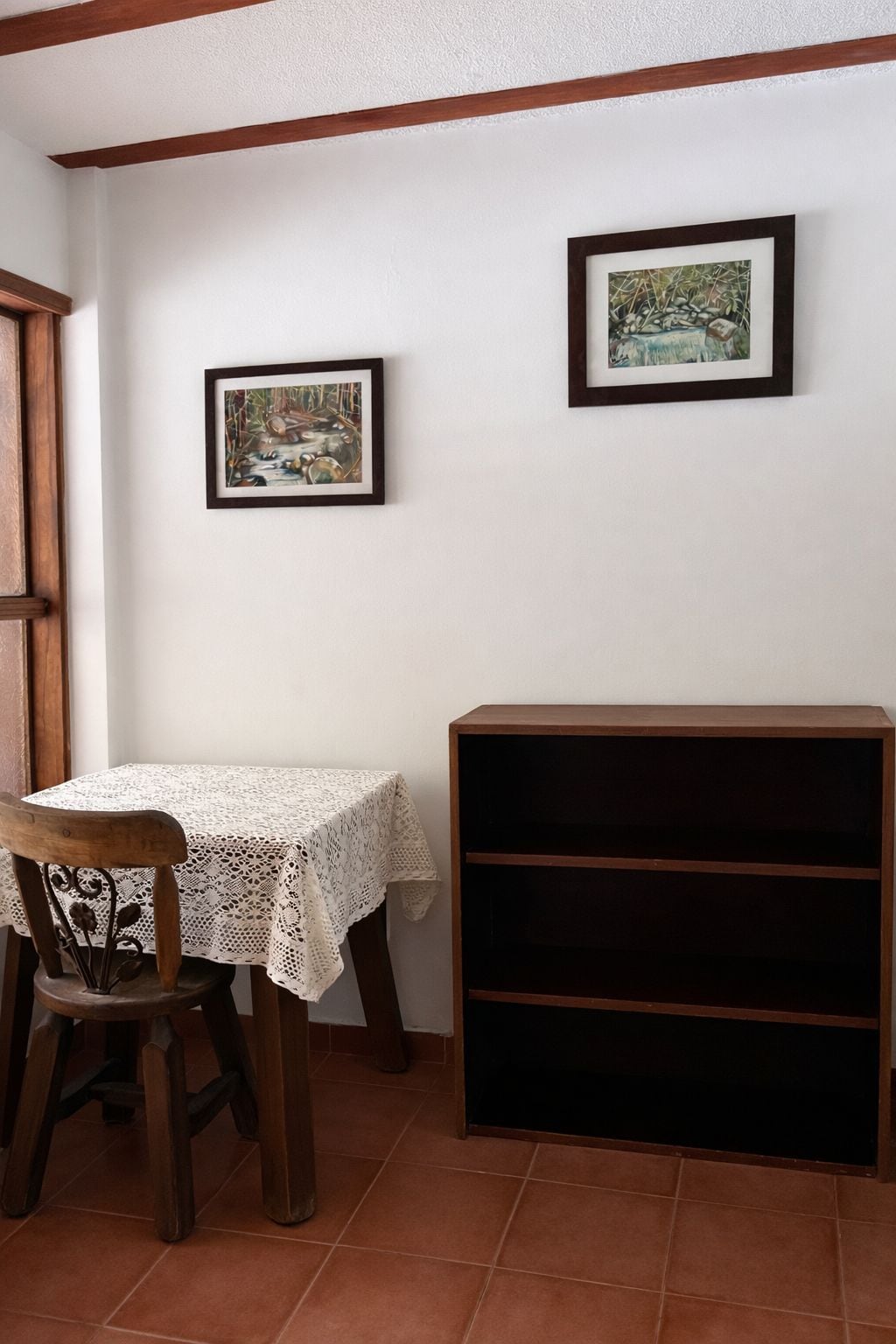 Un comedor con una mesa y sillas, una estantería y dos cuadros en la pared.