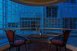 A corner seating area with two chairs and a table, a bottle of wine, and a view through a window with a grid pattern.
