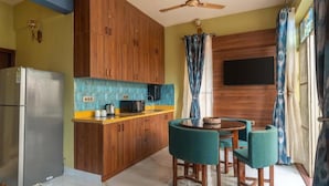 A compact kitchen with wooden cabinets, a refrigerator, a microwave, and a small dining area with two chairs. - Casa Albela (Bengaluru)