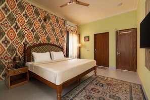 A bedroom with a bed, nightstand, lamp, patterned wall, ceiling fan, and two doors.