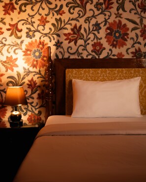 A bed with a headboard, a bedside lamp, and a wall with floral wallpaper.