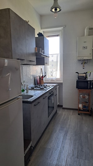 Una cucina con piano cottura, forno e microonde integrati. Una finestra offre vista sull'esterno.