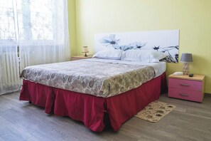 Un dormitori amb llit, una taula de nit, una làmpada i un moble d'estriar de color rosa.