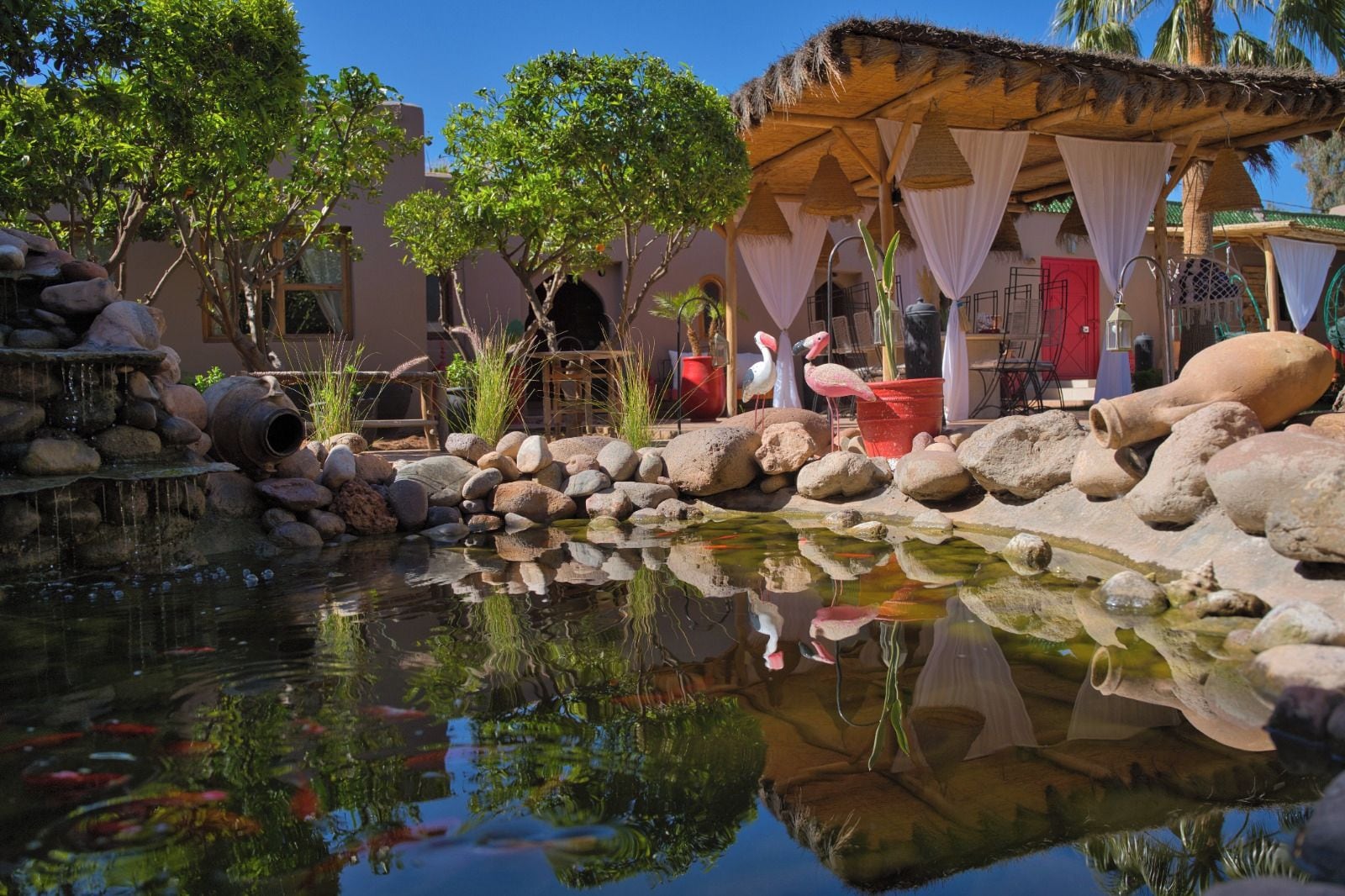 A tranquil outdoor area with a pond, rocks, and a thatched-roof structure.