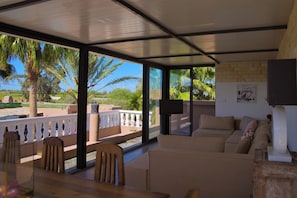 A modern living room with a large window overlooking a pool and palm trees, a sofa, and a flat-screen TV.