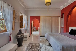 Ein Schlafzimmer mit einem Bett, einer großen Vase, einem gemusterten Teppich und Blick auf einen Essbereich.