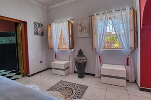 Ein Zimmer mit Fliesenboden, einer großen Vase und zwei mit Vorhängen versehenen Fenstern.