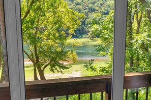 A view from a wooden deck overlooking a river with trees and a grassy area. - Serenity by the Lake 3BR Home (Branson)