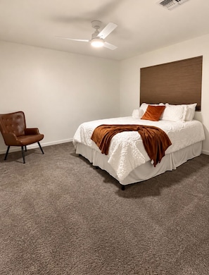 Quarto com cama, cadeira, ventoinha no teto e janela com persianas.