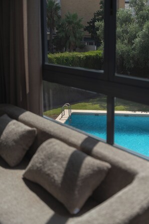 A view of a swimming pool from a window with a sofa and cushions in the foreground. - Sun-Soaked Haven | Pool & Just Steps from the Beach (Alicante)