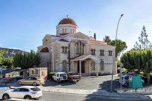 A church with a dome and a bell tower, surrounded by parked cars and trees. - Troodos View Garden House - Trimiklini (Trimiklini)
