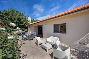 A patio area with a table and chairs, a white bathtub, and a window overlooking a garden with roses. - Troodos View Garden House - Trimiklini (Trimiklini)