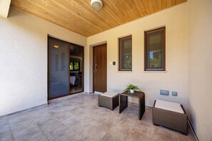 A covered patio area with a sliding glass door leading to an interior space, a small table with a plant, and a wicker chair. - Troodos View Garden House - Trimiklini (Trimiklini)