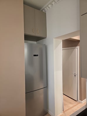 Eine kompakte Küche mit einem eingebauten, edelstahlfarbenen Kühlschrank, einer Holz Arbeitsplatte und einer weißen Tür zu einem anderen Raum.