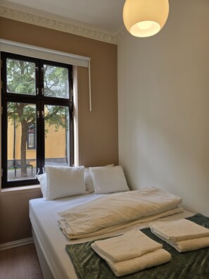 Ein Hotelzimmer mit Bett, Kissen, einem Fenster mit Blick auf die Straße und einer Hängelampe.