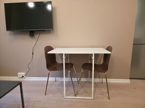 Ein Zimmer mit einem weißen Tisch, zwei braunen Stühlen, einem an der Wand montierten Flachbildfernseher und einer weißen Steckdose.