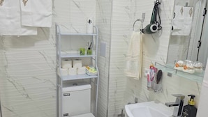 Een badkamer met toilet, wastafel, spiegel en een plank met toiletartikelen.