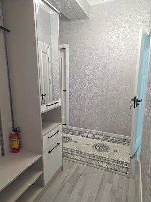A room with a wardrobe, a mirror, a door, a patterned rug, and a fire extinguisher.