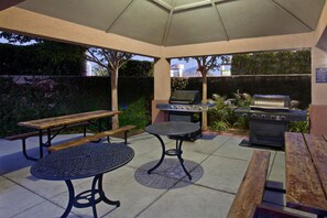 Eine Terrasse im Freien mit Grill, rundem Tisch und Bank.
