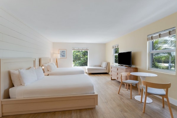 Hotellihuone, jossa on kaksi sänkyä, televisio, pieni ruokapöytä ja tuolit.