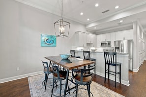 A modern kitchen with white cabinets, stainless steel appliances, and a dining area with a wooden table and chairs. - 400 Ocean Blvd-  3-bedroom condo steps from pier and village (St. Simons Island)