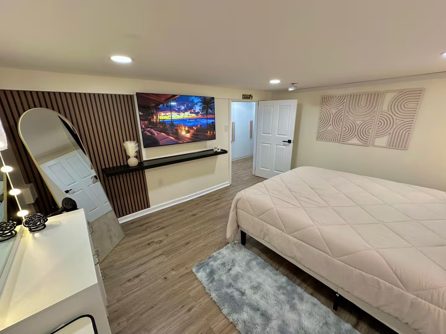 A bedroom with a bed, a vanity with a mirror, a television, and a door leading to another room.