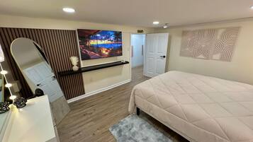A bedroom with a bed, a vanity with a mirror, a television, and a door leading to another room.