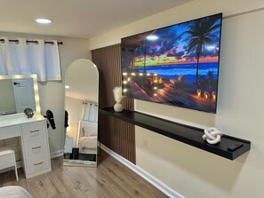 A modern bedroom with a large TV displaying a sunset scene, a vanity with lights, and a bed with a view of the room.