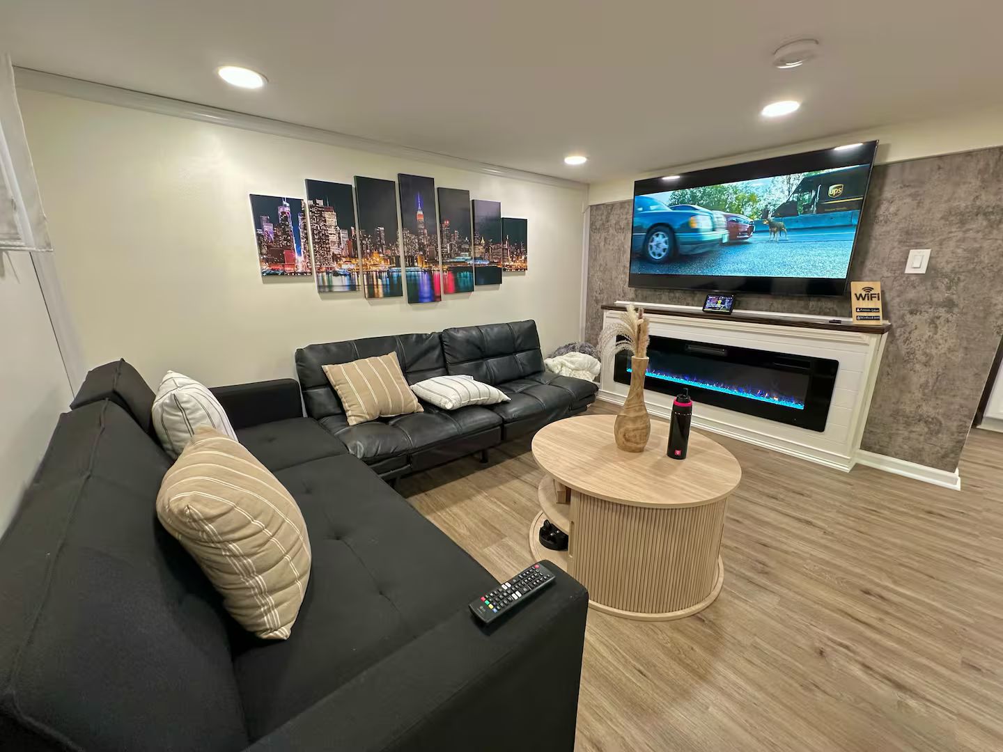 Uma sala de estar moderna com sofá seccional, televisão de tela plana, lareira e um mural com vista para a cidade.