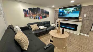 Uma sala de estar moderna com sofá seccional, televisão de tela plana, lareira e um mural com vista para a cidade.