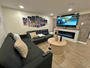 Una sala moderna con un sofá seccional, un televisor de pantalla plana, una chimenea y un mural con vista a la ciudad.
