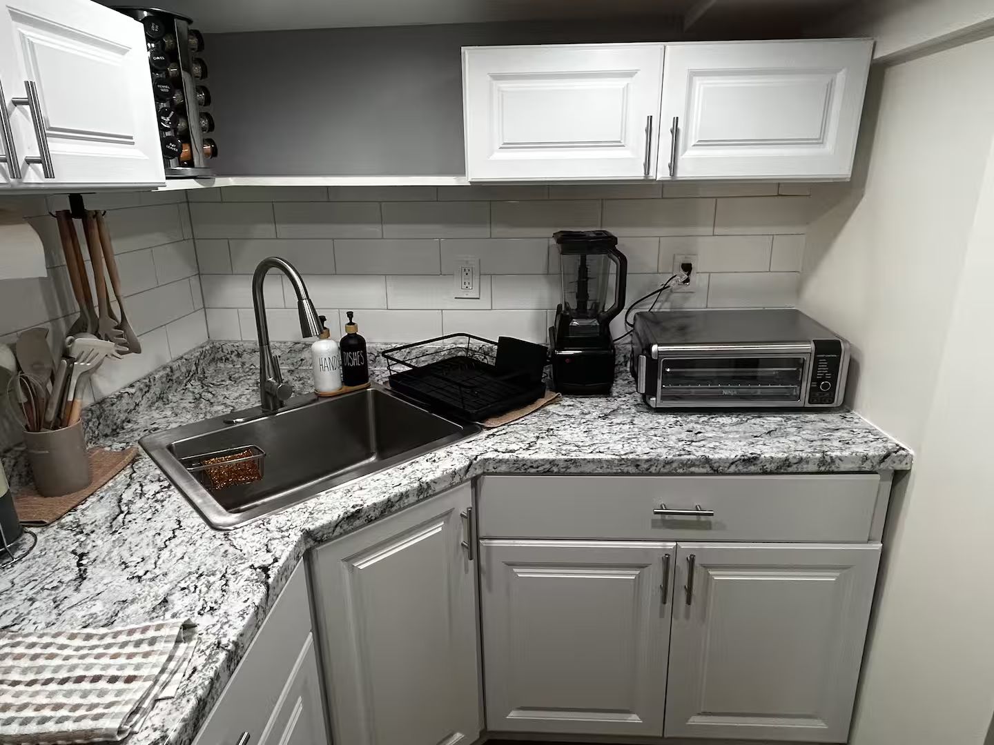 Una cocina con armarios blancos, encimera de granito, pileta, cafetera y tostadora.