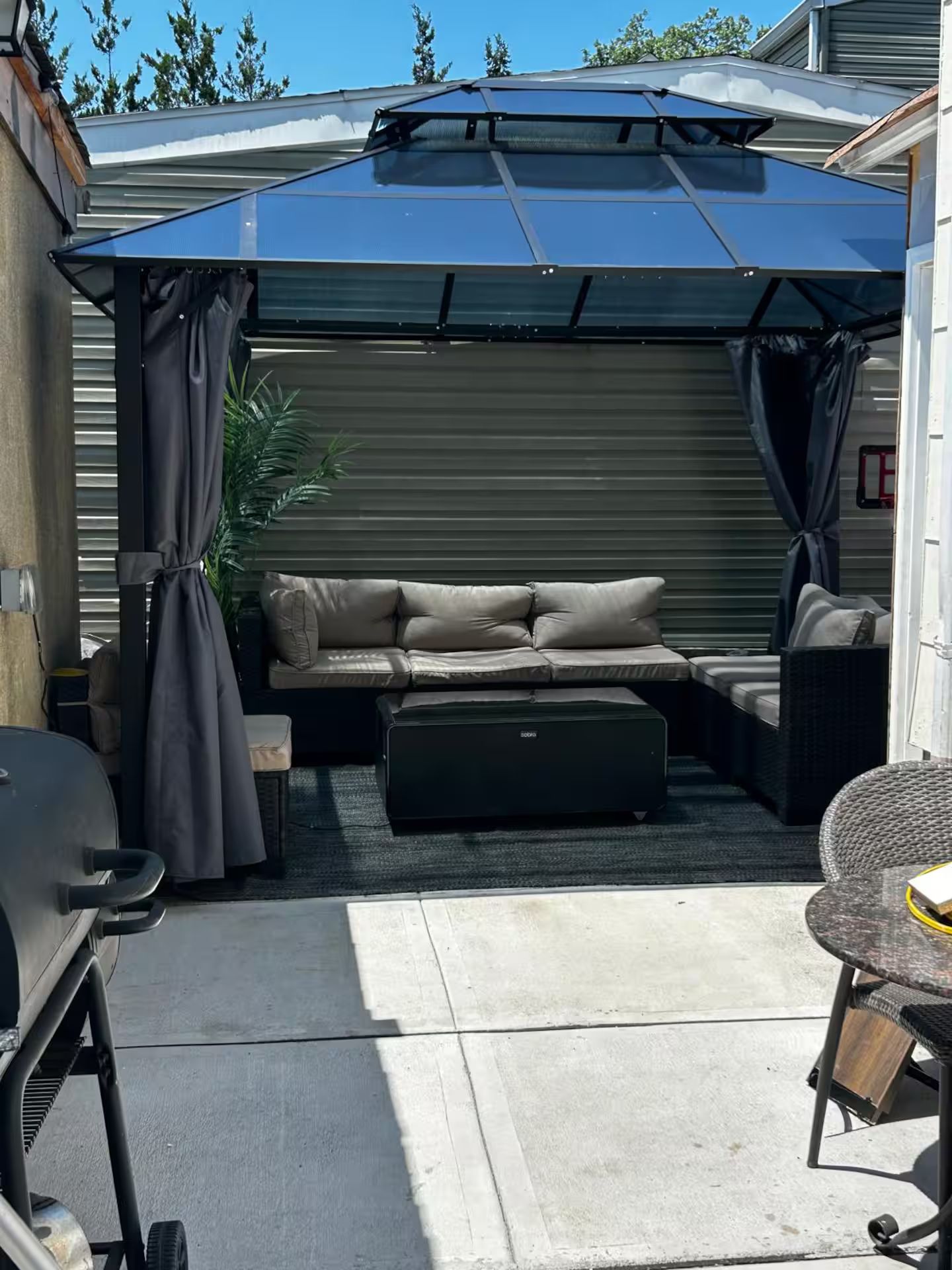 A covered outdoor seating area with a sofa and chairs, a grill, and a patio umbrella.