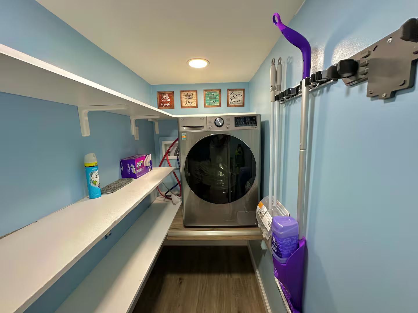 A laundry room with a front-loading washing machine, shelves with laundry supplies, and a wall-mounted drying rack.
