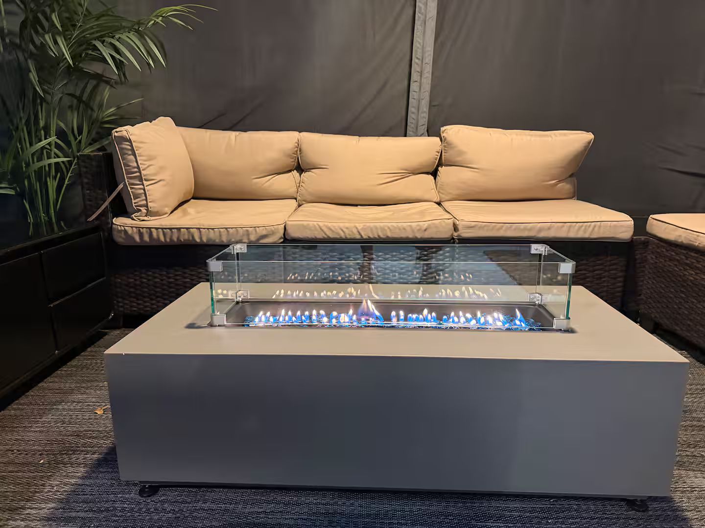Un soggiorno moderno con un divano beige, un tavolino con piano in vetro e una fiamma blu, e una pianta in vaso.