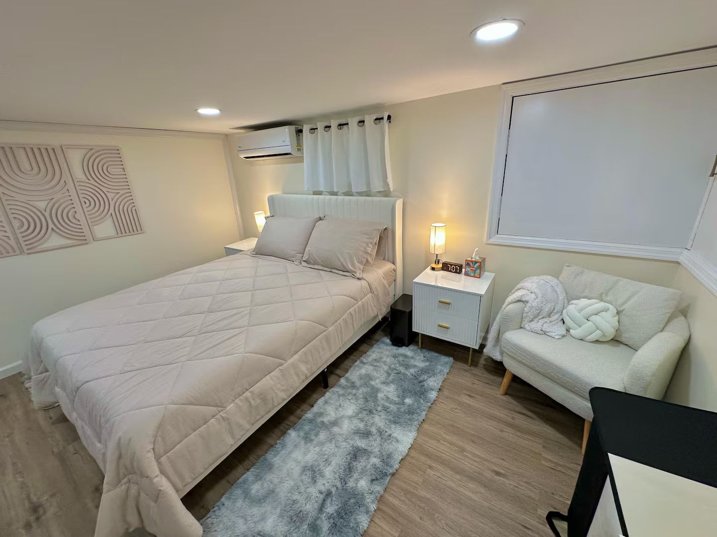 Un dormitorio con cama, mesitas de noche, sofá y aire acondicionado instalado en la pared.