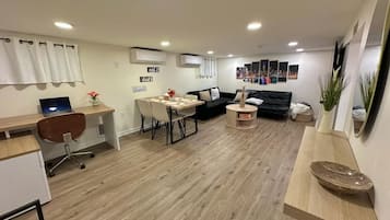 Um espaço de estar moderno com área de jantar, sofá de couro preto, mesa de centro de madeira e um laptop em uma escrivaninha.