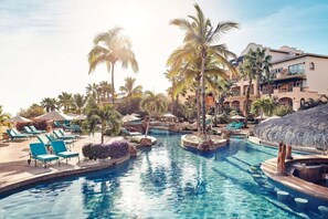 Ein Resort-Pool mit mehreren Bahnen, Palmen und Liegestühlen.