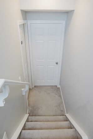 A carpeted staircase leading to a white door with a doorknob. - Modern 1-Bedroom, 1- Bathroom Private Basement Suite in Windermere (Edmonton)