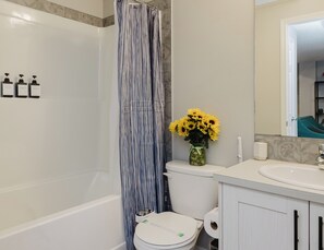 Ein Badezimmer mit Duschvorhang, Toilette, Waschbecken und einer Blumenvase.