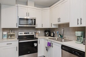 A modern kitchen with white cabinetry, a stainless steel microwave, an oven, a dishwasher, and a coffee maker. - Modern 1-Bedroom, 1- Bathroom Private Basement Suite in Windermere (Edmonton)