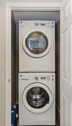 A compact, two-door laundry room with a washing machine and dryer stacked vertically. - Modern 1-Bedroom, 1- Bathroom Private Basement Suite in Windermere (Edmonton)