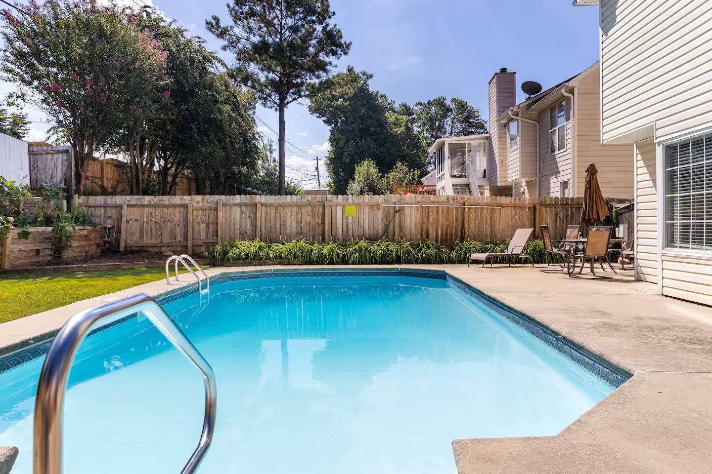 A backyard with a swimming pool, a wooden fence, and a patio with outdoor furniture.
