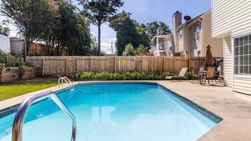 A backyard with a swimming pool, a wooden fence, and a patio with outdoor furniture.